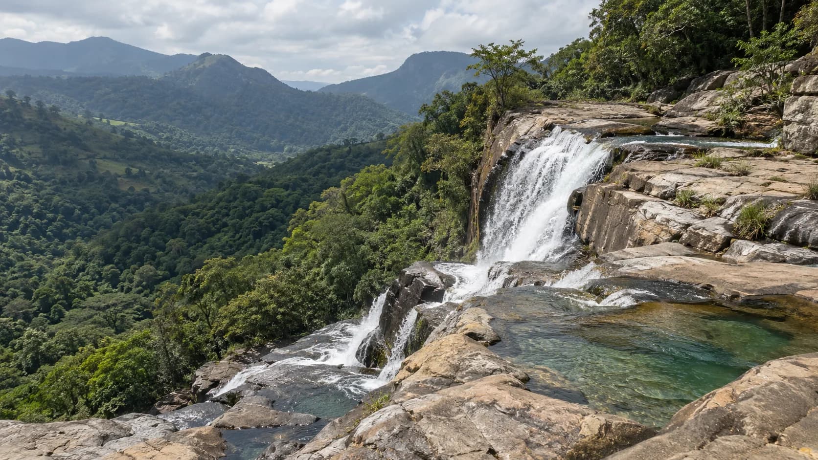 Rocky waterfall and natural pools above a green hill-country valley